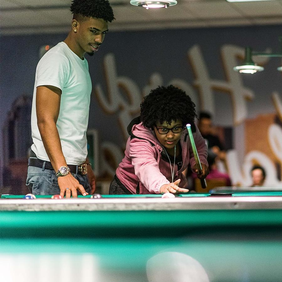 2 students play pool in the game room.